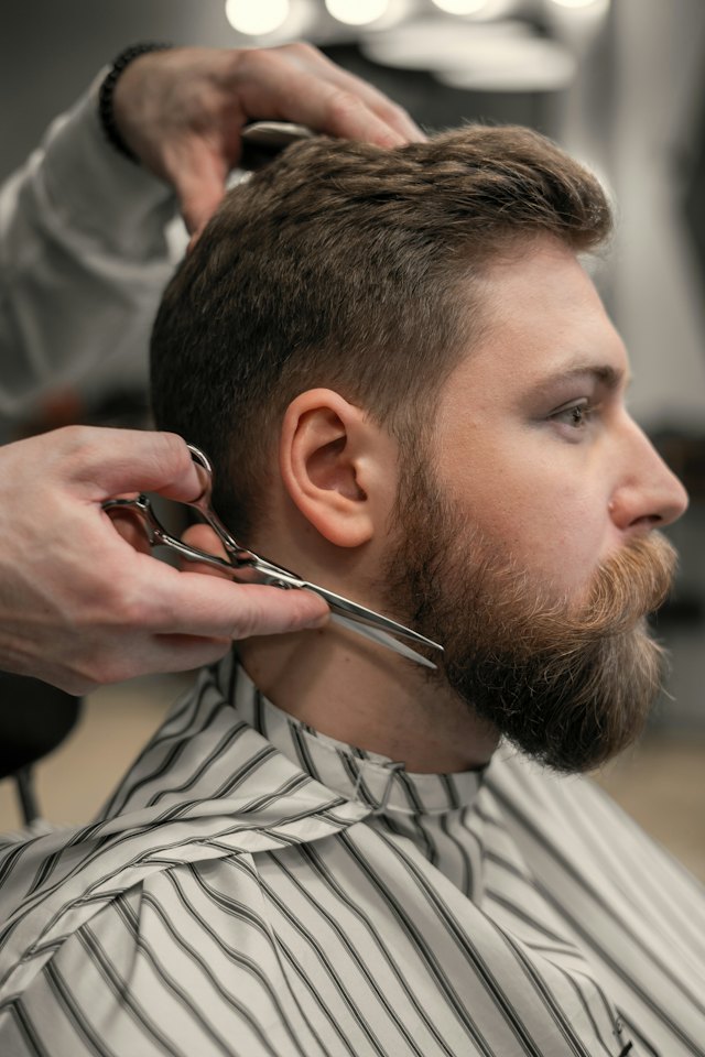 A barber trims a customer's beard with scissors