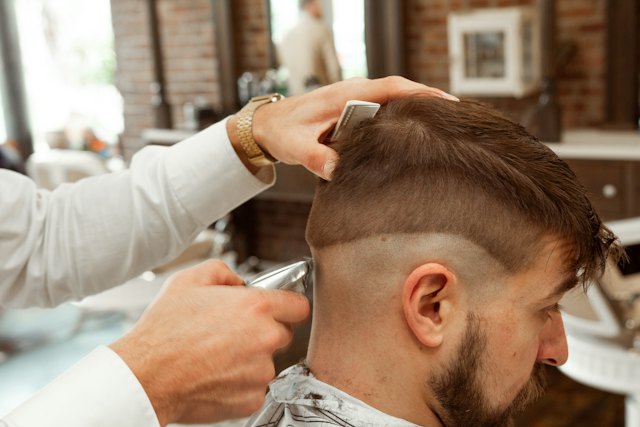 A barber cuts a customer's hair with scissors and a comb